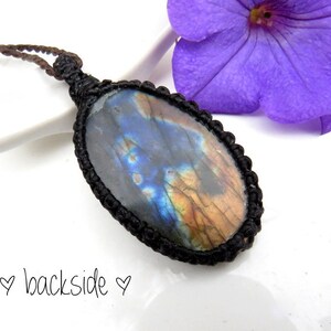 May include: A black cord necklace with an oval-shaped labradorite gemstone pendant. The gemstone has a blue, green, and gold iridescent sheen.