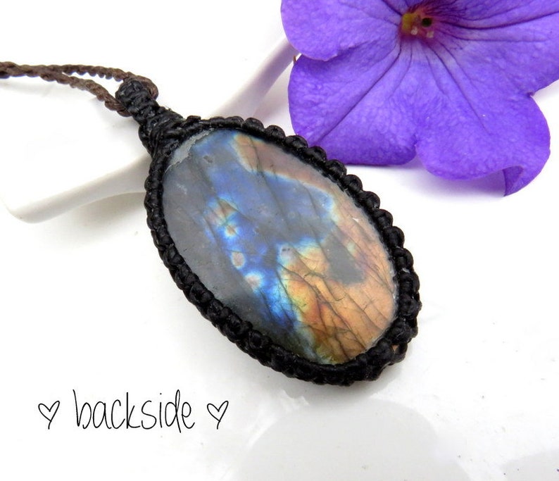 May include: A black cord necklace with an oval-shaped labradorite gemstone pendant. The gemstone has a blue, green, and gold iridescent sheen.