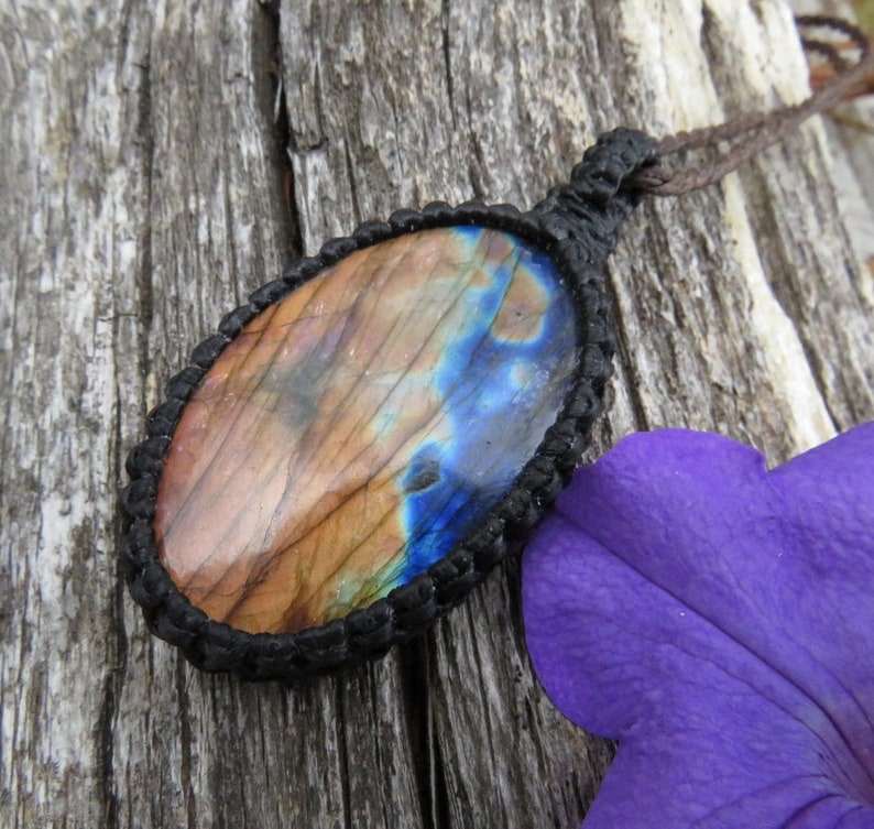 May include: A brown and blue labradorite gemstone pendant with a black cord. The pendant is oval shaped and is set in a black macrame knot.