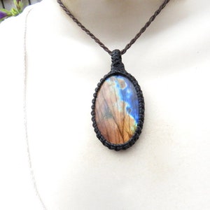 May include: A brown cord necklace with a macrame pendant featuring a blue and brown labradorite gemstone.