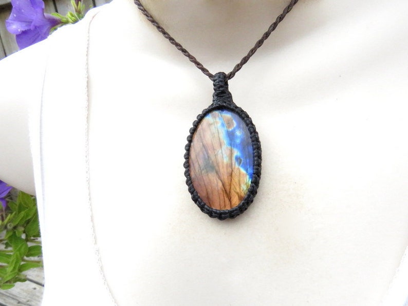 May include: A brown cord necklace with a macrame pendant featuring a blue and brown labradorite gemstone.