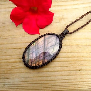 以下が含まれることがあります： 茶色の紐のネックレスに、大きな楕円形のラブラドライトのペンダントがついたもの。ペンダントは薄い茶色で、虹色の紫色と青色の光沢がある。