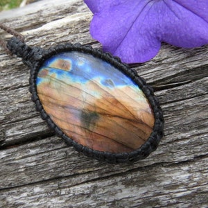 May include: A brown and blue labradorite gemstone pendant with a black cord. The pendant is oval shaped and has a natural, iridescent finish.