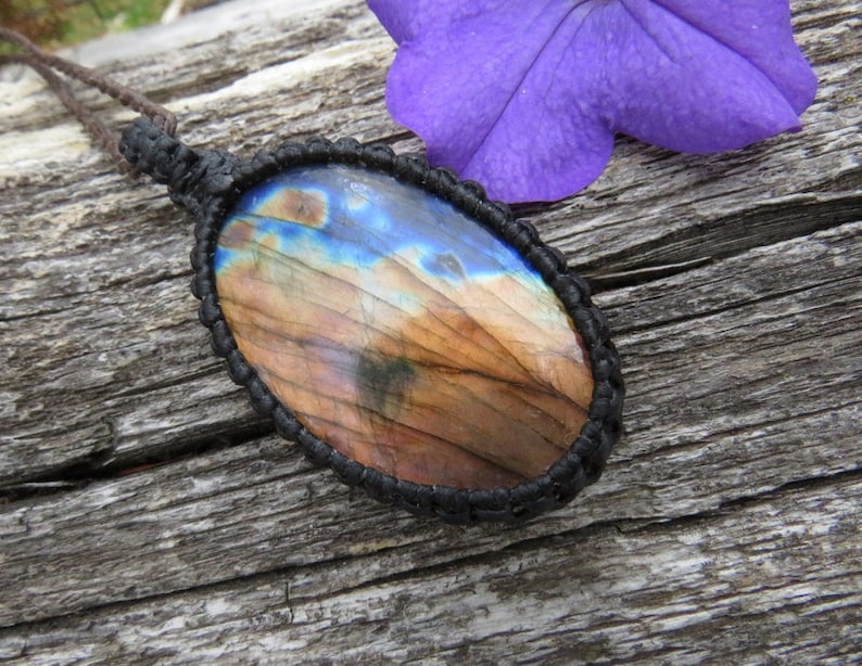May include: A brown and blue labradorite gemstone pendant with a black cord. The pendant is oval shaped and has a natural, iridescent finish.