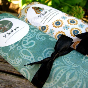 May include: Two rolled up gift wrap tubes with a teal and white paisley pattern and a black ribbon. The tubes have a white circle with a butterfly and the text "Thank you" and a website address. The other tube has a yellow and white floral pattern with the text "Thank you".