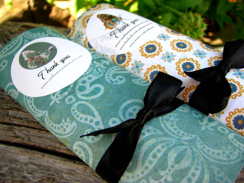 May include: Two rolled up gift wrap tubes with a teal and white paisley pattern and a black ribbon. The tubes have a white circle with a butterfly and the text "Thank you" and a website address. The other tube has a yellow and white floral pattern with the text "Thank you".