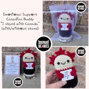 May include: A crocheted Canadian Buddy doll wearing a red shirt with the text "I stand with Canada!" on a white card. The doll is sitting on a wooden stand and is packaged in a white organza bag. The doll is a handmade emotional support Canadian buddy.