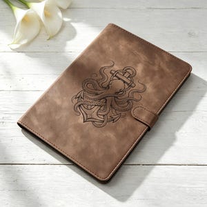 Pode incluir: Uma capa de caderno retangular castanha com uma aba de fecho magnético. A parte frontal apresenta uma ilustração gravada em castanho escuro de um polvo enrolado à volta de uma âncora náutica. A capa tem costuras visíveis nas extremidades.