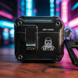 May include: Black protective case for Airpods with the text "JOHN'S AIRPODS" and a graphic of a person wearing a gas mask. The case has a latch that says "OPEN" and a key ring attachment.