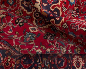 May include: Close-up of a rolled-up, ornate red rug with a detailed floral pattern. The rug features a deep red background with accents of navy blue, cream, and teal. The intricate design suggests a traditional, handcrafted style.