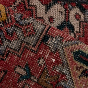 May include: Close-up of a section of a vintage rug with a detailed, woven pattern. The rug features a rich color palette of red, beige, yellow, and blue. The design includes geometric shapes and floral motifs, showcasing a traditional style.