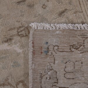 May include: Close-up of a beige rug with a fringe border. The rug has a subtle pattern of faded floral designs.