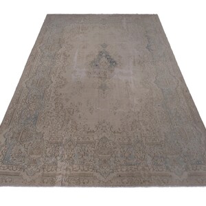 May include: A vintage rug with a faded floral pattern in shades of beige and blue. The rug has a worn and distressed look, giving it a rustic and antique feel.
