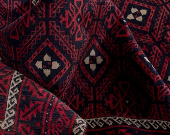 May include: Close-up of a folded rug with a detailed geometric pattern. The rug features a deep navy blue background with intricate red and beige designs. The pattern includes diamond shapes and floral motifs, creating a rich, textured appearance.