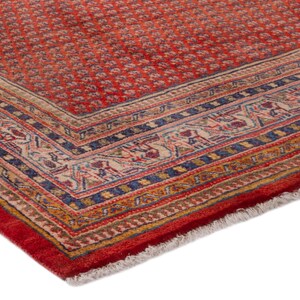 Puede incluir: Esquina de una alfombra oriental roja con un patr&oacute;n floral detallado. La alfombra tiene un borde con dise&ntilde;os intrincados en azul, beige y dorado. El borde de la alfombra est&aacute; terminado con flecos.