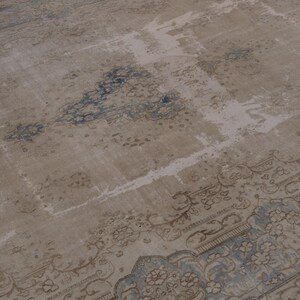 May include: A vintage rug with a faded, light brown background and a blue and brown floral pattern. The rug has a distressed look with some areas of wear and tear.
