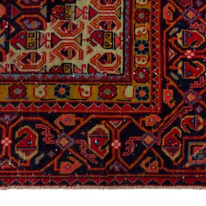 May include: Close-up of a section of a traditional oriental rug. The rug features a complex geometric pattern in shades of red, navy blue, gold, and green. The border has a repeating design, and the rug has a fringed edge.