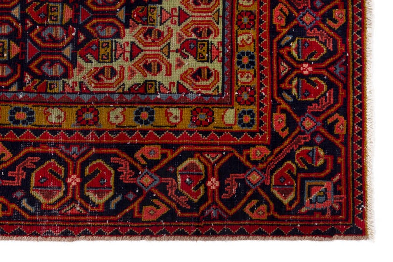 May include: Close-up of a section of a traditional oriental rug. The rug features a complex geometric pattern in shades of red, navy blue, gold, and green. The border has a repeating design, and the rug has a fringed edge.