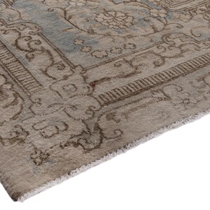 May include: Close-up of the edge of a light brown rug with a faded blue and brown floral pattern. The rug has a fringe border.