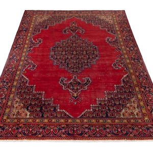 May include: A large, rectangular red rug with an intricate, ornate design. The rug features a central medallion and detailed borders in navy blue, gold, and brown. The rug's pattern is symmetrical, with a traditional, vintage aesthetic.