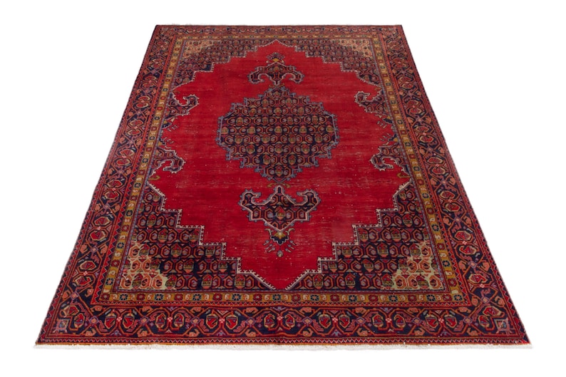May include: A large, rectangular red rug with an intricate, ornate design. The rug features a central medallion and detailed borders in navy blue, gold, and brown. The rug's pattern is symmetrical, with a traditional, vintage aesthetic.