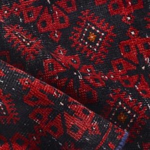 May include: Close-up of a red and black patterned rug with a geometric design. The rug has a textured surface and is made of a woven material.