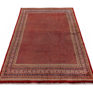 Puede incluir: Una alfombra rectangular roja con un patr&oacute;n detallado. La alfombra tiene un campo central de peque&ntilde;os motivos repetidos, enmarcado por un borde con dise&ntilde;os intrincados en beige, negro y rojo. Los bordes de la alfombra est&aacute;n acabados con flecos.