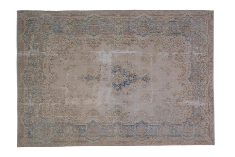 May include: A vintage rug with a faded beige background and a blue and beige patterned border. The rug has a worn and distressed look, giving it a rustic and antique feel.