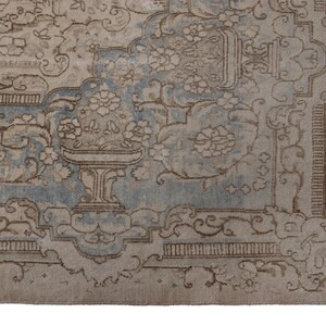 May include: A vintage rug with a light blue and beige color scheme. The rug features a floral pattern with intricate details. The rug has a worn and faded look, giving it a vintage aesthetic.