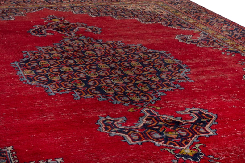 May include: A vibrant red area rug with intricate geometric patterns in navy blue, gold, and light blue. The rug features a central medallion design and detailed borders, showcasing a traditional aesthetic. The rug's texture appears slightly distressed.