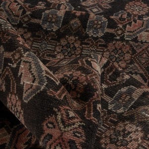 Peut inclure: Gros plan sur un tapis enroulé avec un motif complexe. Le tapis présente un fond marron foncé avec des motifs géométriques et floraux détaillés en rouge, beige et bleu. La texture semble douce et tissée.