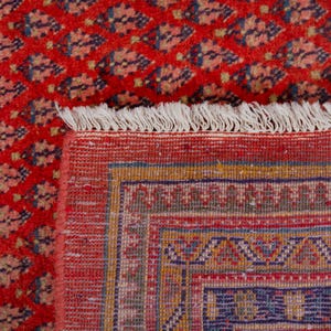Puede incluir: Primer plano de una alfombra oriental roja con un patr&oacute;n detallado. La alfombra presenta un dise&ntilde;o floral repetido en tonos azules y beige. El borde tiene patrones geom&eacute;tricos y flecos.