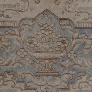 May include: A vintage rug with a light blue and beige floral pattern. The rug features a central design of a vase with flowers.