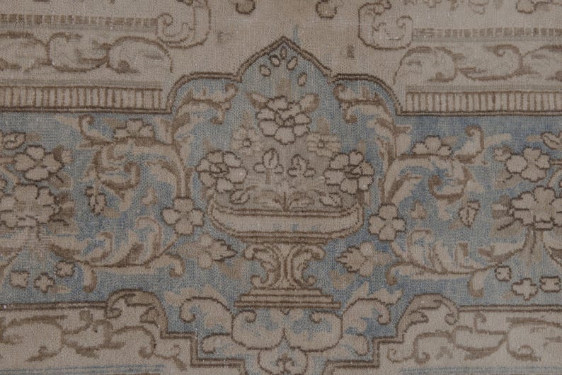 May include: A vintage rug with a light blue and beige floral pattern. The rug features a central design of a vase with flowers.
