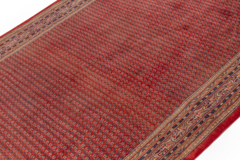 Puede incluir: Una alfombra roja estampada con un borde detallado. La alfombra tiene un patr&oacute;n floral repetido en un color rojo m&aacute;s oscuro. El borde presenta un dise&ntilde;o complejo con tonos de azul, beige y rojo. La alfombra es rectangular.