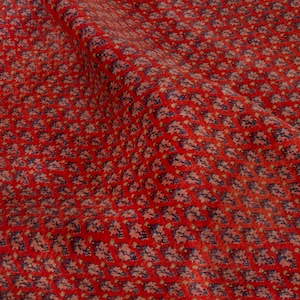 Puede incluir: Primer plano de una tela roja con un estampado floral repetitivo. El patr&oacute;n presenta peque&ntilde;as flores estilizadas en tonos beige y azul, sobre un fondo rojo vibrante. La tela est&aacute; ligeramente drapeada, mostrando su textura y profundidad.