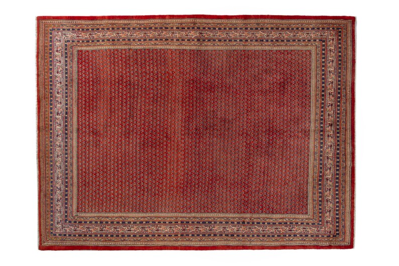 Puede incluir: Una alfombra oriental rectangular roja con un borde detallado. La alfombra presenta un campo central rojo con un patr&oacute;n repetitivo. El borde es una mezcla de beige, azul y negro, con dise&ntilde;os intrincados. La alfombra probablemente est&aacute; hecha de lana o un material similar.