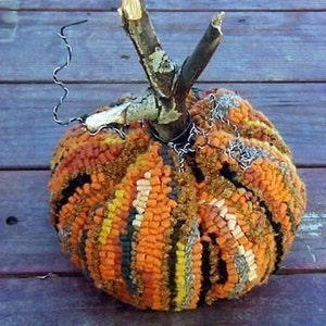 Peut inclure: Une citrouille colorée, cousue à la main, en laine et en chutes de tissu. La citrouille a une tige rustique en bois naturel et est décorée d'une chaîne en fil de fer.