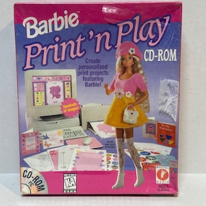 May include: A Barbie Print 'n Play CD-ROM box. The box is pink and blue, featuring a Barbie doll in a pink top and yellow skirt. The text on the box reads "Barbie Print 'n Play" and "Create personalized print projects featuring Barbie!"