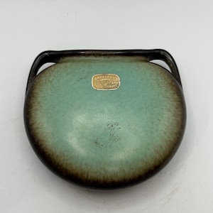 May include: A small, round, ceramic dish with a turquoise center and a dark brown rim. The dish has two small handles and a gold foil label that reads "Carstens Tönnieshof Germany".