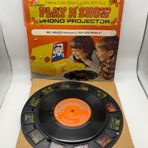 May include: Vintage Kenner's Play N' Show Phono Projector box set. The orange and yellow box features the text "Talking Color Show For Use With Your PLAY N SHOW PHONO PROJECTOR". The set includes a black record with a series of small images around the edge.