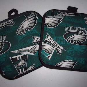 May include: Two green and black pot holders with a Philadelphia Eagles theme. The pot holders feature the team logo and the words "Eagles" and "Philadelphia".