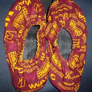 May include: A pair of maroon fabric shoe covers with a yellow and white print. The print features the words "Washington" and "Commanders" repeated throughout.