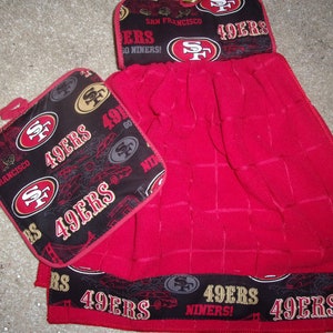 May include: A red kitchen towel with a black and gold trim featuring the San Francisco 49ers logo and the text "49ers" and "Niners!"  The towel comes with a matching pot holder.