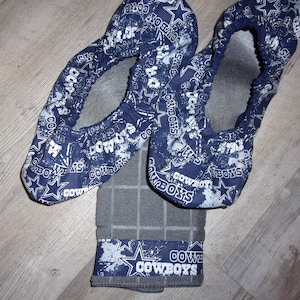 May include: Two blue and white fabric shoe covers with a Dallas Cowboys theme. The covers have a white star and the words "Cowboys" printed on them. A gray and white checkered fabric with a blue and white Cowboys band is also included.