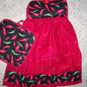 May include: Red kitchen towel with a chili pepper print. The towel has a pocket for a matching pot holder. The pot holder is also red with a chili pepper print.