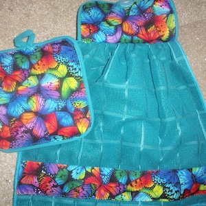May include: Teal kitchen towel with a butterfly print. The towel has a hanging loop and a matching pot holder.
