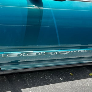 May include: A teal green car with a black bumper and side molding. The car has a white "DOHC VTEC" decal on the side.