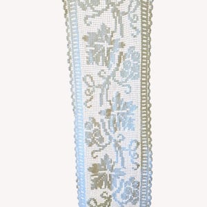 May include: A rectangular, off-white lace table runner with a floral design. The runner features a detailed pattern of flowers and vines, with a scalloped edge. The lace is delicate and appears to be handmade, adding a vintage or antique aesthetic.