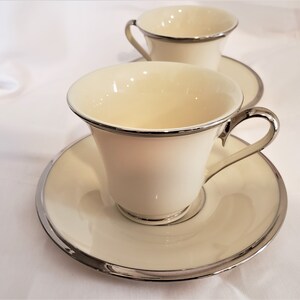 May include: Two white porcelain teacups with silver trim and matching saucers. The cups have a classic design and are perfect for a formal tea party.